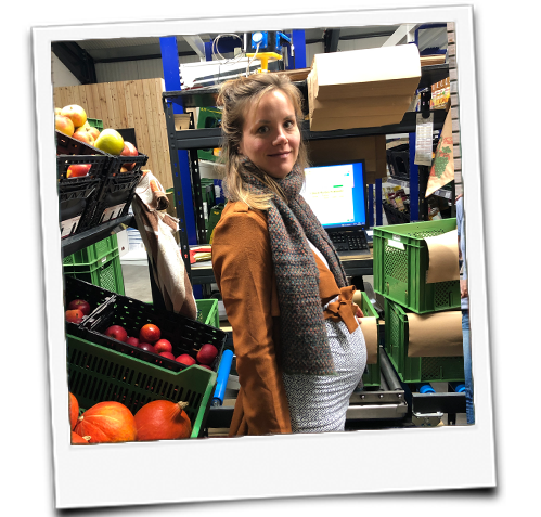 KI generiert: Eine Person steht in einem Obstlager voller Kisten mit Äpfeln und Kürbissen.