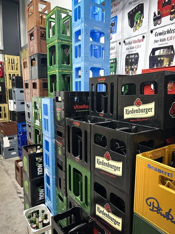 KI generiert: Gestapelte Getränkekisten, Marken: Voelkel, Riedenburger. Poster mit Preisen und Produkten im Hintergrund.
