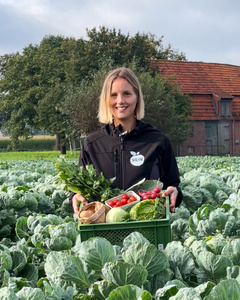 Frau mit Gemüsekiste steht auf einem Feld. Auf Jacke der Schriftzug "MOIN".