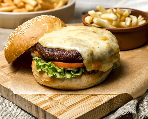 KI generiert: Ein Hamburger mit geschmolzenem Käse, Tomate, Salat; Beilage: Pommes.