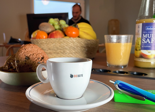 KI generiert: Auf dem Tisch stehen eine Tasse, Obst, Orangensaft und Kekse. Text: "BIOBOTE".