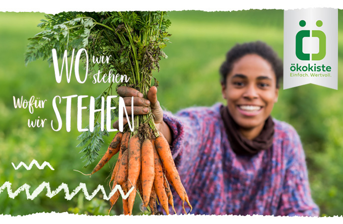 KI generiert: Frau hält Karotten in einem Feld. Text: "WO wir stehen, Wofür wir STEHEN". Ökokiste-Logo rechts oben.
