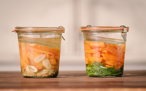 KI generiert: Zwei Einmachgläser mit eingelegtem Gemüse, darunter Karotten, Kräuter und Gewürze.