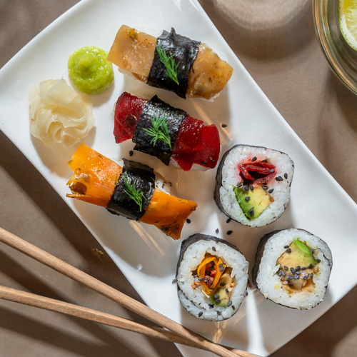 KI generiert: Vegan Sushi auf weißem Teller, dekoriert mit Wasabi und Ingwer, daneben Essstäbchen.
