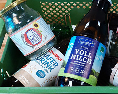 KI generiert: Eine Kiste mit verschiedenen Bio-Getränken und -Produkten. Texte: "Sonnenblumenkerne", "Hafer Drink", "Vollmilch".