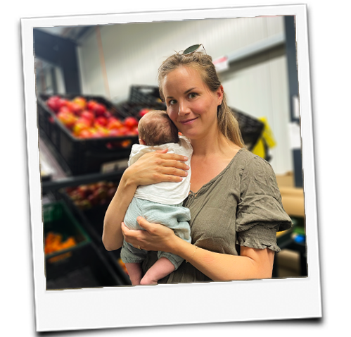 KI generiert: Eine Person hält ein Baby in einer Umgebung mit Obstkisten.