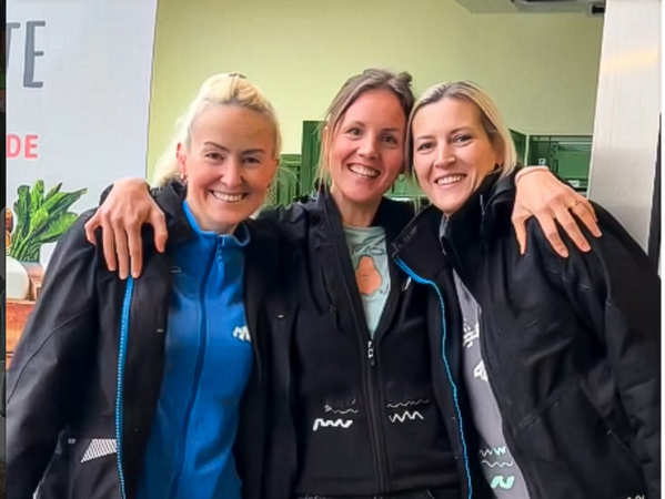 KI generiert: Drei Personen lächeln und haben ihre Arme umeinander gelegt. Links im Bild sind Pflanzen zu sehen.