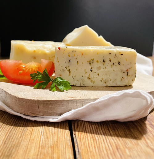 KI generiert: Ein Brett mit Käsestücken, frischer Tomate und Petersilie.