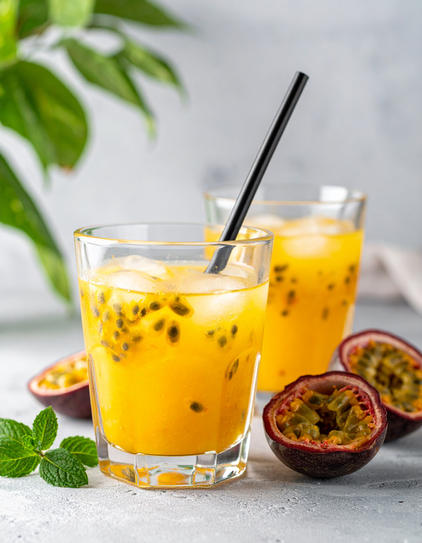 KI generiert: Passionsfrucht-Getränk mit Eiswürfeln im Glas, umgeben von halben Passionsfrüchten und Minzblättern.