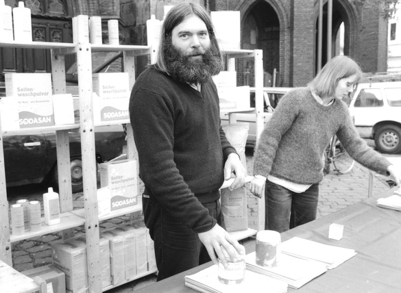 KI generiert: Ein Stand mit Sodasan-Produkten, an dem zwei Personen arbeiten. Text: "Seifenwaschpulver", "SODASAN".