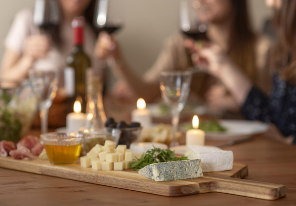 KI generiert: Ein Brett mit verschiedenen Käsesorten, Oliven und Honig, umgeben von Kerzen und Weingläsern.