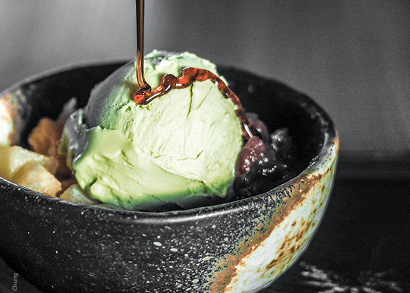 KI generiert: Grüne Eiskugel in Schale mit Soße darüber, serviert mit Obststücken.