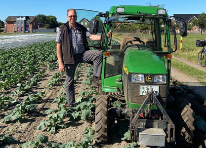 Ein Mann steht neben einem grünen Traktor auf einem Feld.