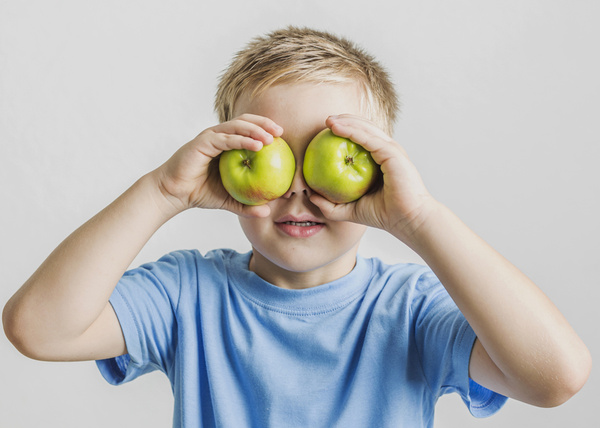 KI generiert: Ein Kind hält zwei grüne Äpfel vor seine Augen.