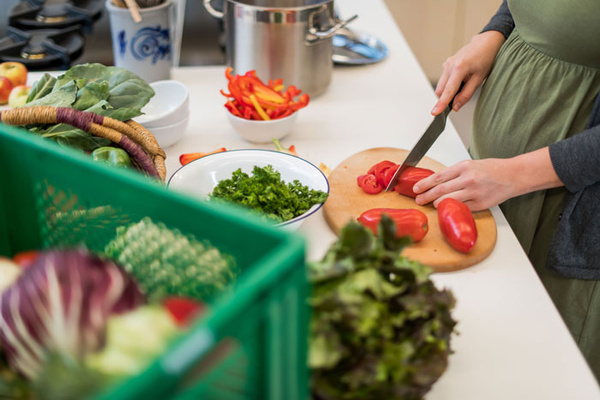 schwangere Frau schnibbelt Gemüpse in der Küche