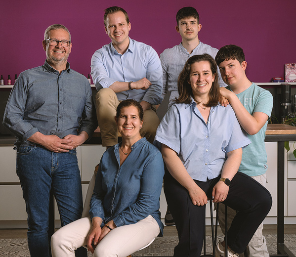 KI generiert: Eine Gruppe von sechs Personen posiert für ein Foto vor einer lila Wand. Keine Textelemente erkennbar.