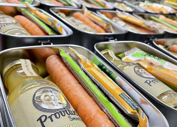 KI generiert: Befüllte Lunchboxen mit Saftflaschen, Karotten und Müsliriegeln. Text: "Wir machen Bio aus Liebe".