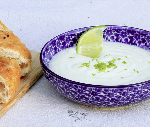 KI generiert: Lila Schale mit Joghurt und Limettenscheibe, daneben ein Stück Brot auf Holzbrett.