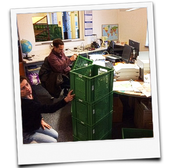 KI generiert: Zwei Personen neben einem Stapel grüner Kisten im Büro.