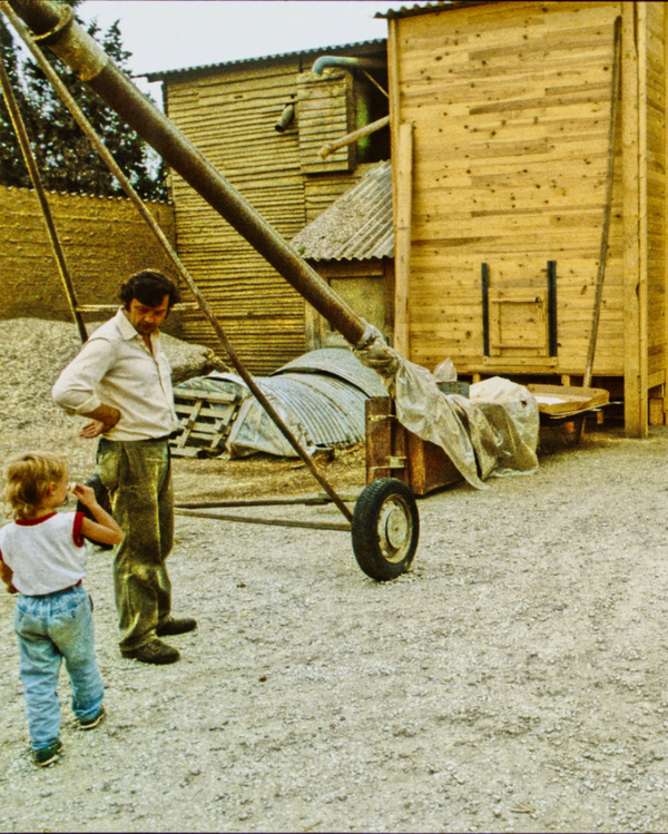 KI generiert: Ein Mann und ein Kind stehen vor einer landwirtschaftlichen Maschine auf einem Hof.