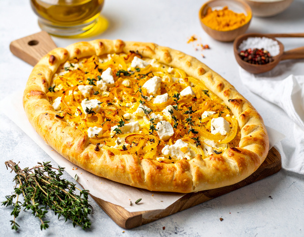 KI generiert: Eine rustikale Pizza mit Feta, Kürbis und Kräutern auf einem Holzbrett.