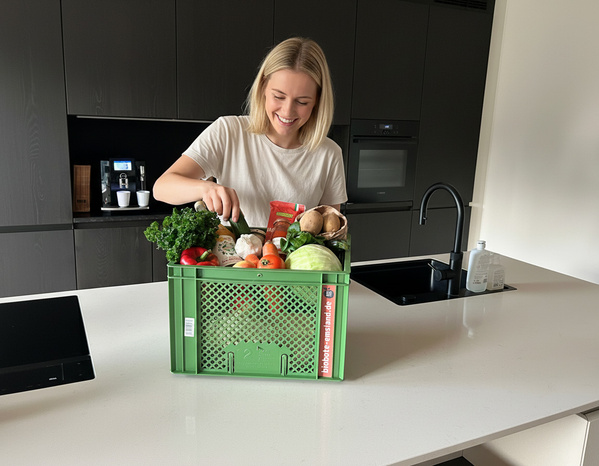 KI generiert: Eine Frau sortiert frisches Gemüse aus einer grünen Kiste in ihrer Küche. Text: "biokiste-eosland.de".