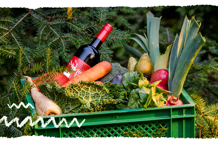 KI generiert: Grüne Kiste mit Gemüse, Obst und einer Weinflasche im Freien. Keine weiteren Textelemente.