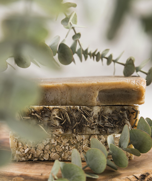 KI generiert: Zwei handgefertigte Seifenstücke mit natürlichen Zutaten auf einem Holzbrett, umgeben von Eukalyptusblättern.