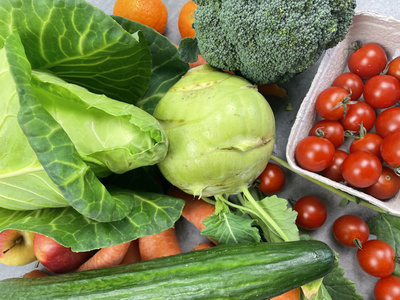 KI generiert: Das Bild zeigt eine Auswahl an frischem Gemüse und Obst, darunter Kohlrabi, Brokkoli, Tomaten, Gurke, Karotten, Kopfsalat und Orangen. Die lebendigen Farben betonen die Frische und Vielfalt der Lebensmittel.