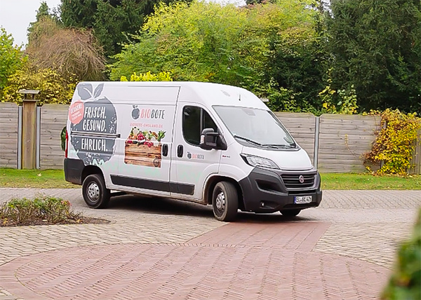 KI generiert: Ein Lieferwagen mit der Aufschrift "FRISCH. GESUND. EHRLICH." steht auf einer gepflasterten Einfahrt.
