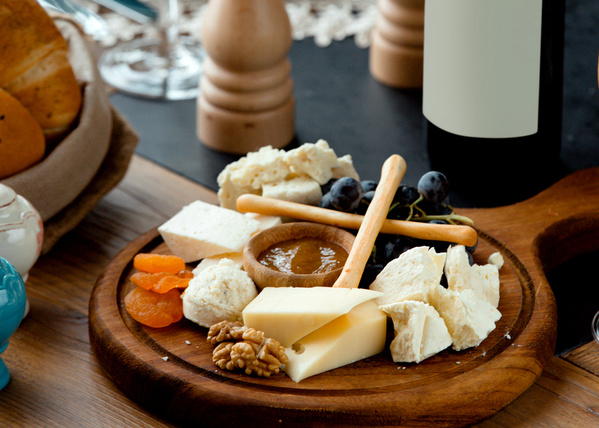 KI generiert: Ein Holzbrett mit Käse, Nüssen, getrockneten Aprikosen, Trauben und einer Honigschale.